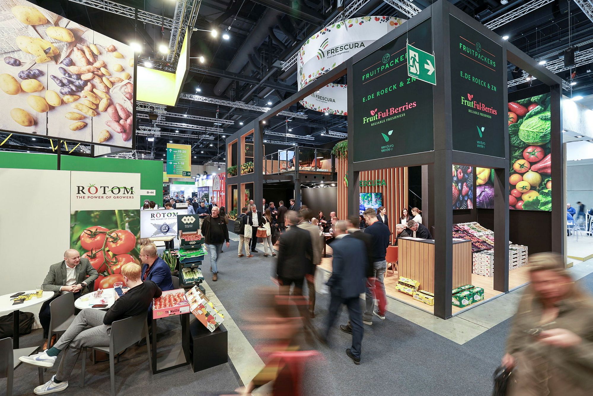 Visitors passing exhibitor stands displaying fresh fruit and vegetables in a trade fair hall.